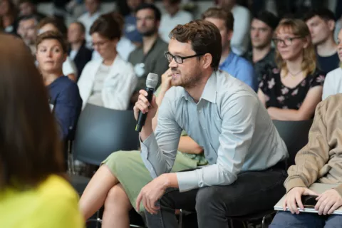 Ein Mann mit einem Mikrofon in der Hand, der im Publikum sitzt und während einer Konferenz eine Frage stellt.