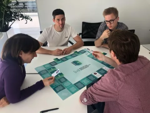 vier Personen sitzen an einem Tisch und spielen ein Brettspiel zu künstlicher Intelligenz
