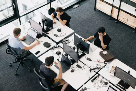 4 Menschen die an Schreibtischen in einem Büro sitzen und arbeiten.