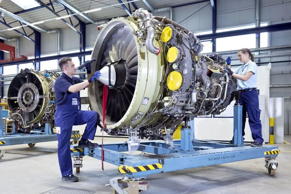 Zwei MechanikerInnen arbeiten an einer alleinstehenden Flugzeugturbine in einer Halle