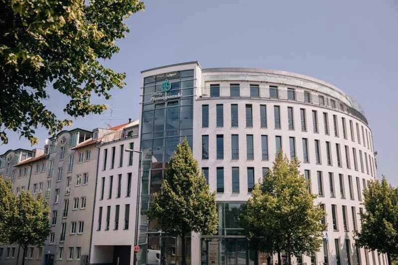 rundliches Bürogebäude in der Stadt mit Bäumen davor.