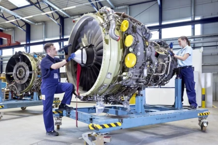 Zwei MechanikerInnen arbeiten an einer alleinstehenden Flugzeugturbine in einer Halle